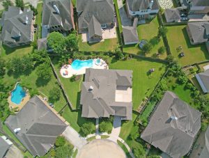 Aerial view of a suburban neighborhood in Houston featuring modern houses with large backyards, lush green lawns, and private swimming pools, ideal for real estate marketing and property tours.