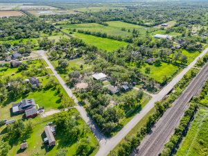 Aerial view of a lush, green residential area in Houston, showcasing rural properties, intersecting roads, and adjacent railway tracks, highlighting real estate opportunities for photography and video tours.