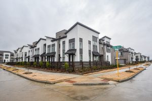 Modern townhouses on a corner lot in Houston, featuring contemporary architecture with white and gray exterior, overcast sky, and well-maintained landscaping. Captured for realtor photography and real estate video tours.